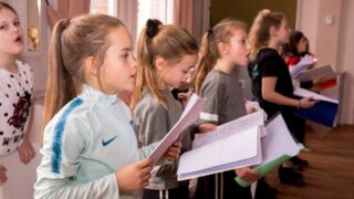 Kinderen die kijken op hun blaadje en aan het zingen zijn.