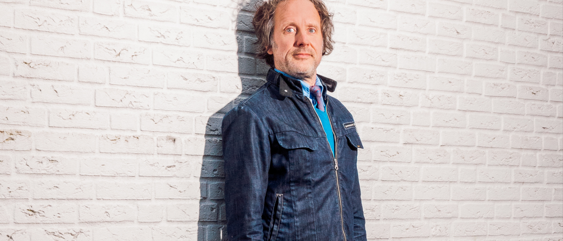 Ronald Snijders voor witte bakstenen muur op promotiefoto voor Leven met humor