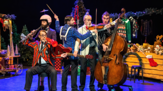 Vijf Släpstick muzikanten in kleurrijke kostuums met diverse instrumenten Ho Ho Kerstshow