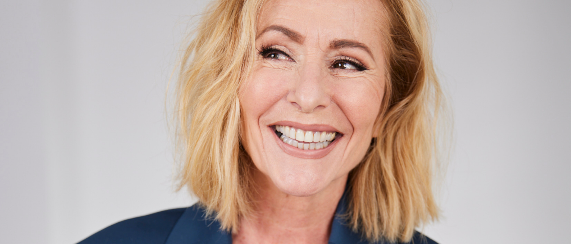 Angela Groothuizen lachend in blauw pak als portretfoto voor theatershow Sexy Sixty