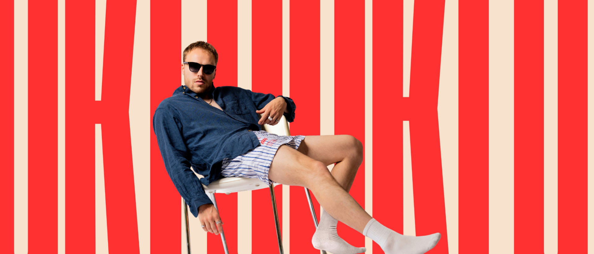 Luuk Weggemans zittend op stoel voor rode typografie, promotiefoto Lach maar om mij