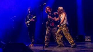 Band rockt met zang en twee gitaren in blauw licht op podium Battle of the Schoolbands 2026